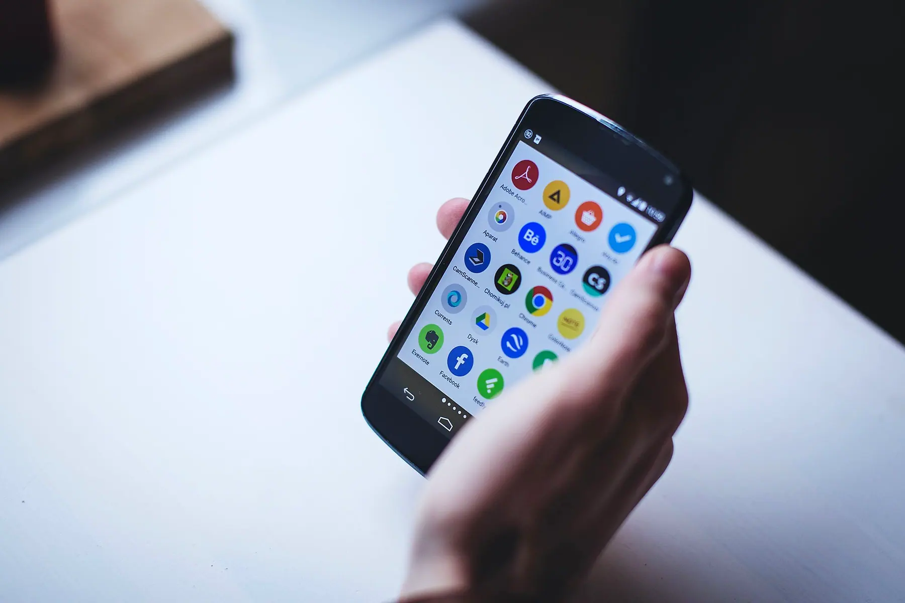 A hand holding a phone with a home screen full of app icons