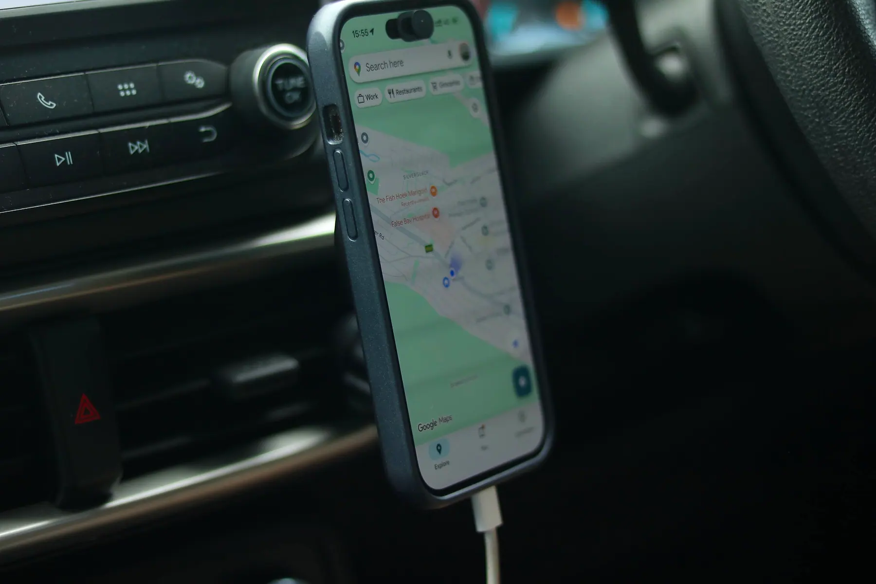 A phone in a car mount showing Google Maps with nearby businesses marked by red pins