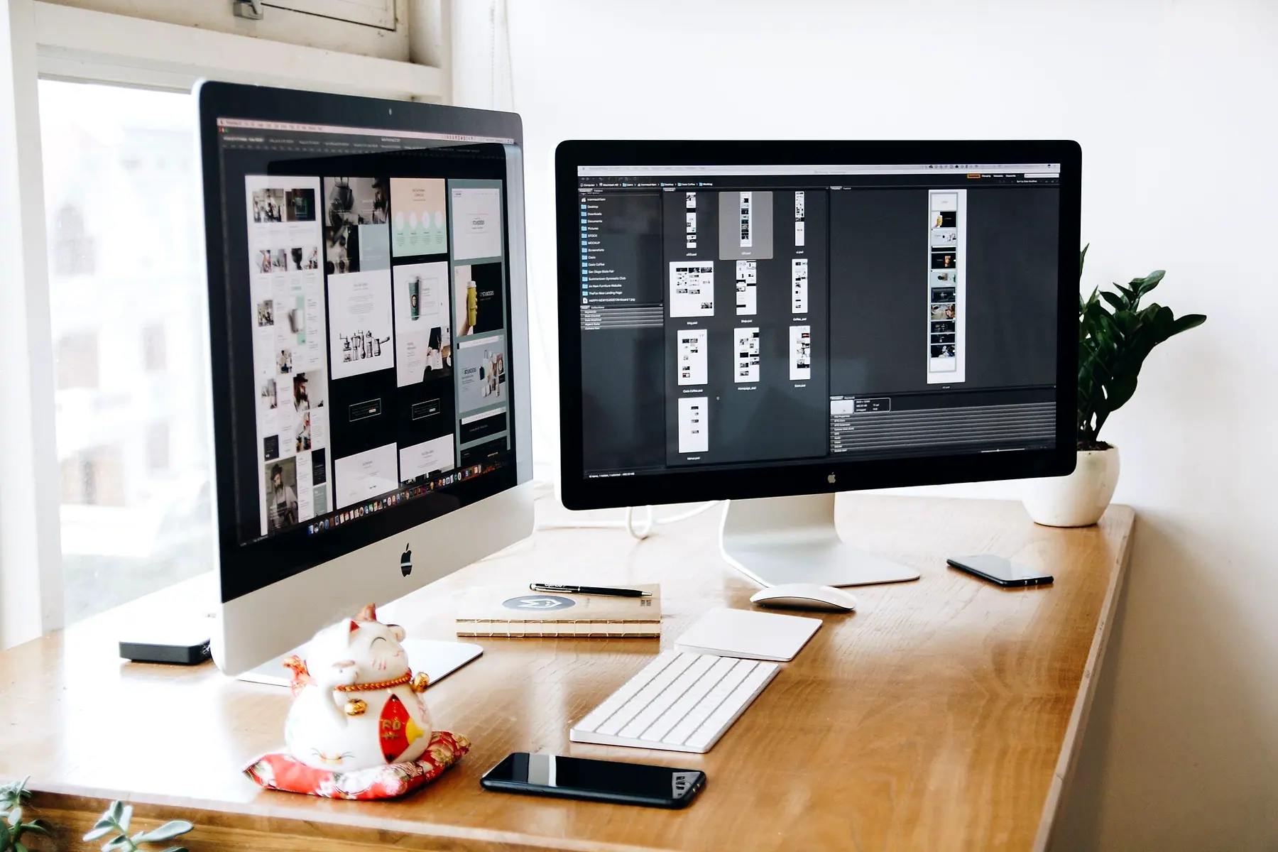 Two desktop monitors on a wooden desk, each showing website page layouts in progress