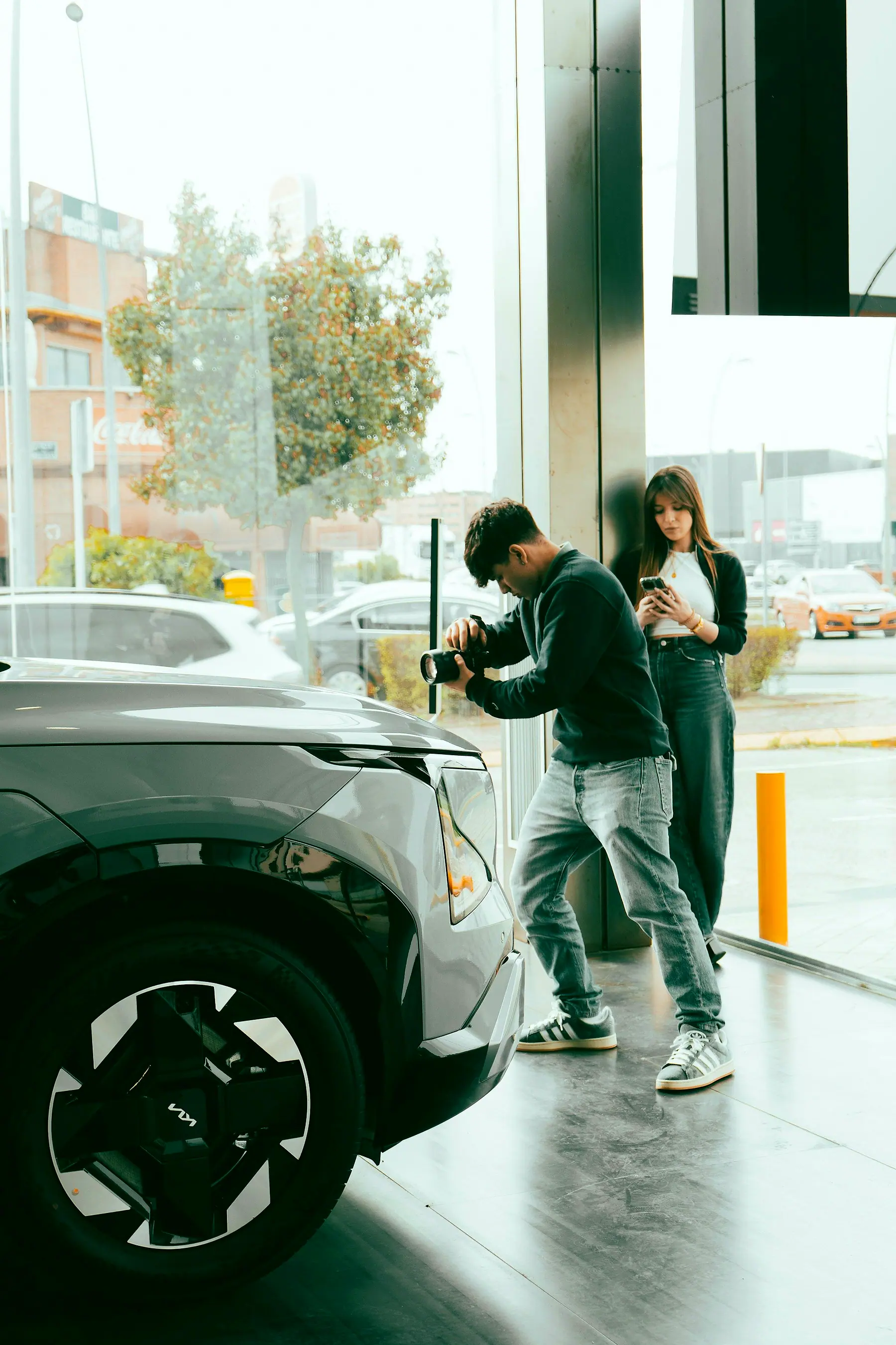 A man photographing a car at a dealership while a woman checks her phone